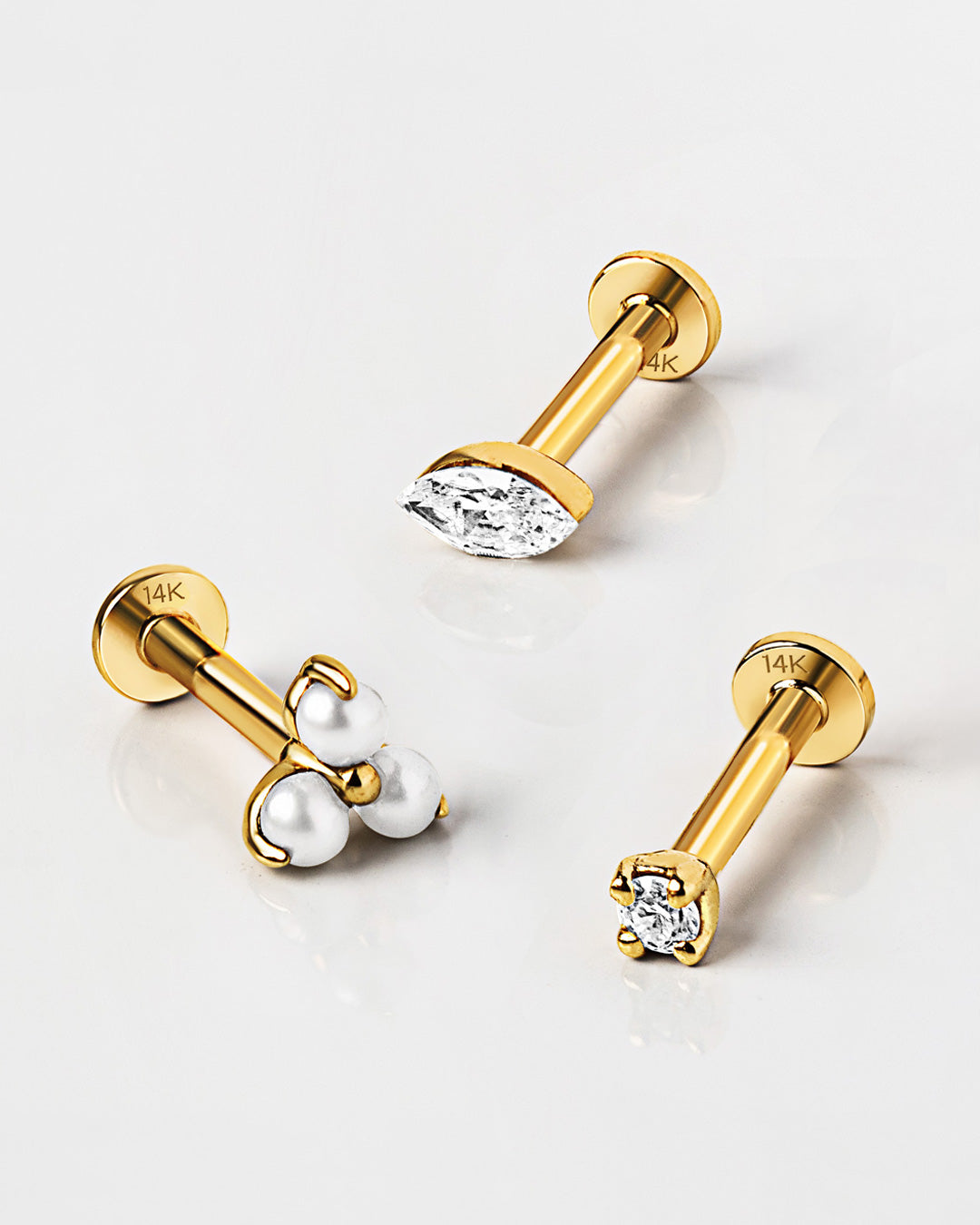Three gold flat back studs on a white surface, one marquise crystal, one three-bead cluster, one round crystal