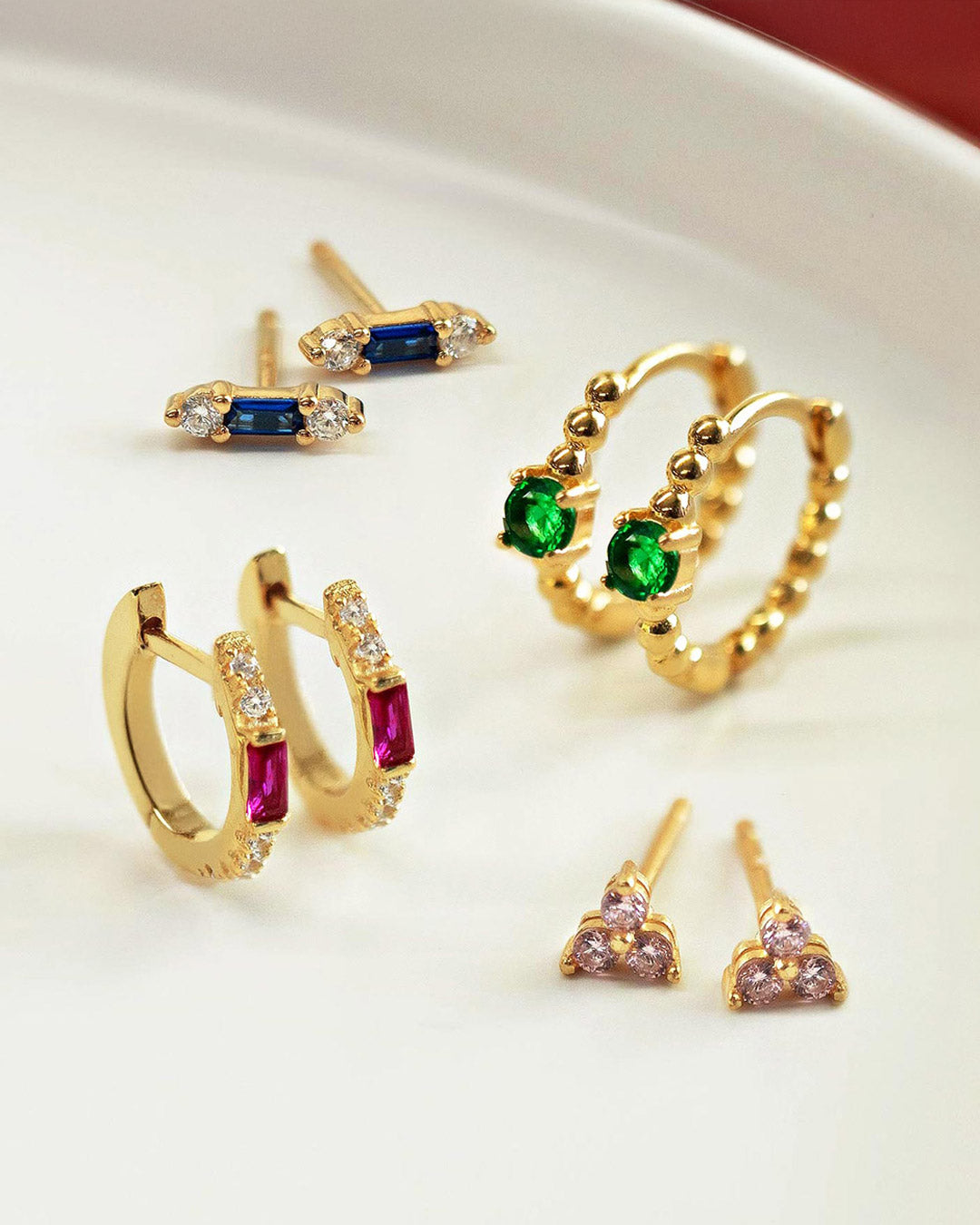 Shop AMYO birthstone jewelry featuring gold earrings with ruby, emerald, sapphire, and pink gemstone details, perfect for meaningful everyday wear and gifting.