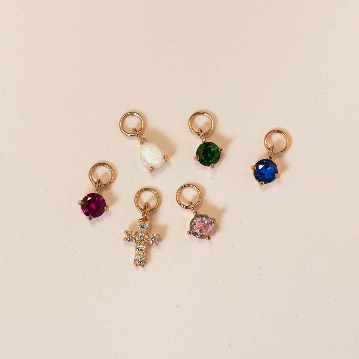 14K gold pear-cut earring charms in opal, green, blue, pink, red and clear stones, on a cream background