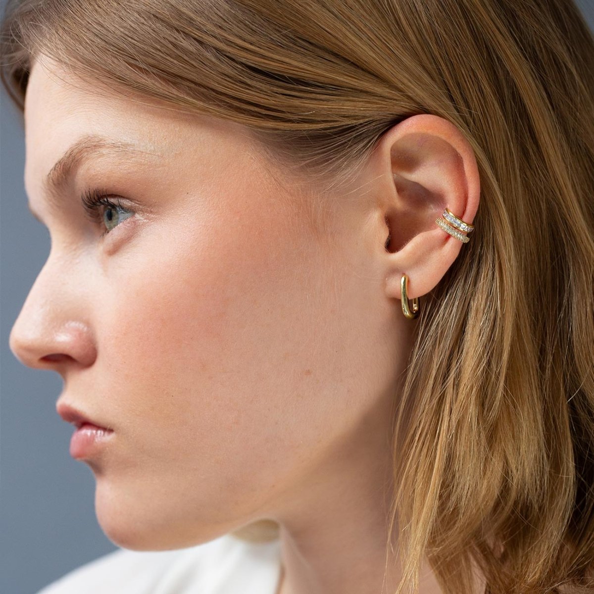 Gold hoop and pavé clear-stone ear cuffs stacked on a model's ear