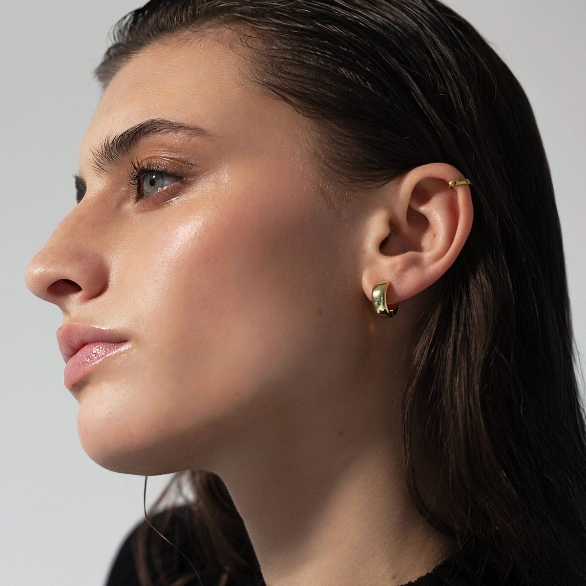 Gold vermeil chunky mini huggie hoop shown on a model's lobe with a plain ear cuff above