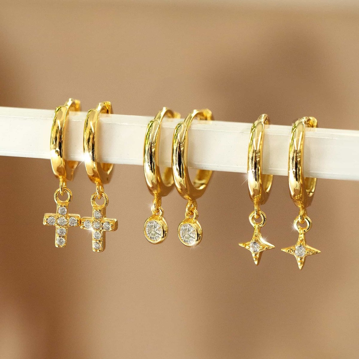 Gold star flare huggie earrings, gold cross dangle huggie earrings, and gold solitaire dangle huggie earrings