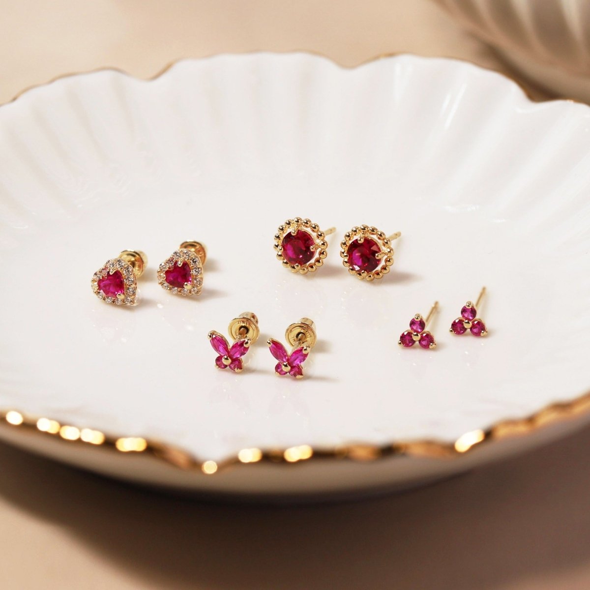 Close up of earrings featuring 14K Gold Gemstone Clover Studs Ruby CZ Crystal and other Ruby gemstone studs