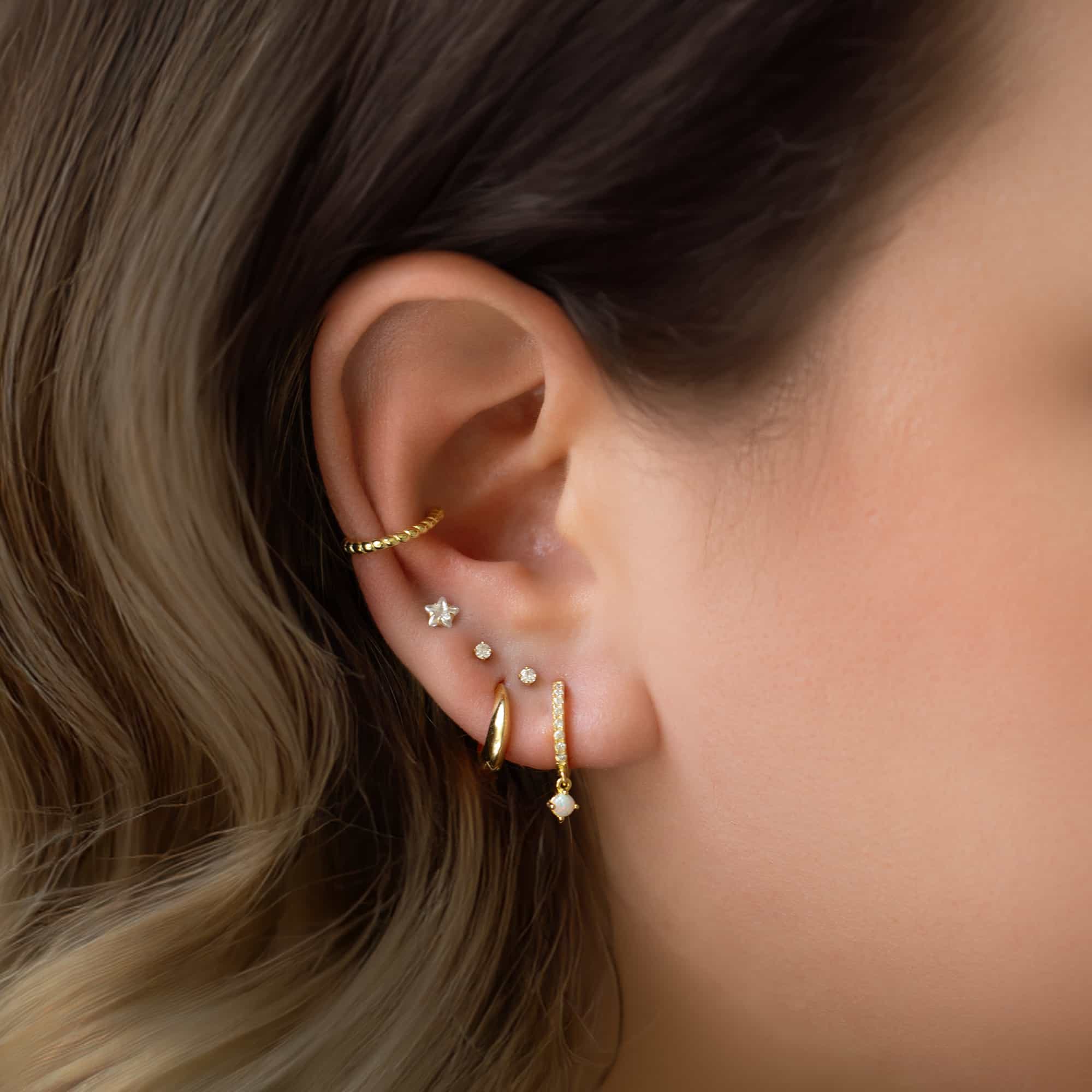 Gold vermeil teardrop huggie hoop shown on a model's lobe, styled in an ear stack