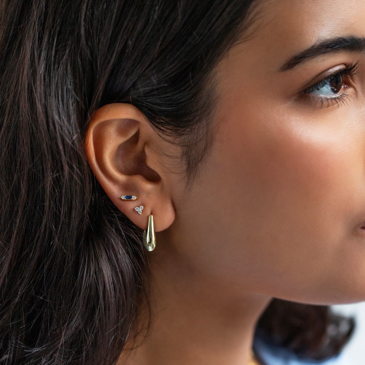 Gold vermeil blue baguette stud with clear accent stones, shown on a model's lobe in an ear stack