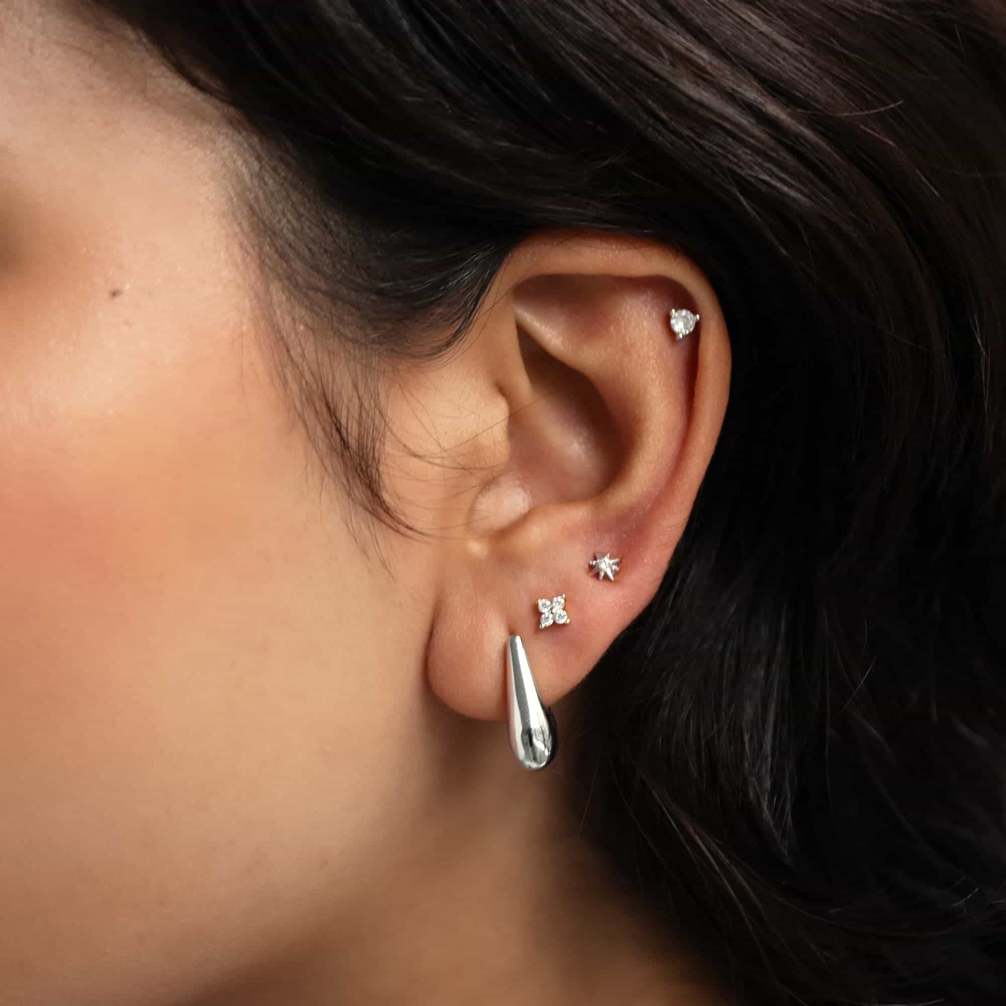 Silver teardrop hoop with star, clover, and clear-stone studs on a model's ear
