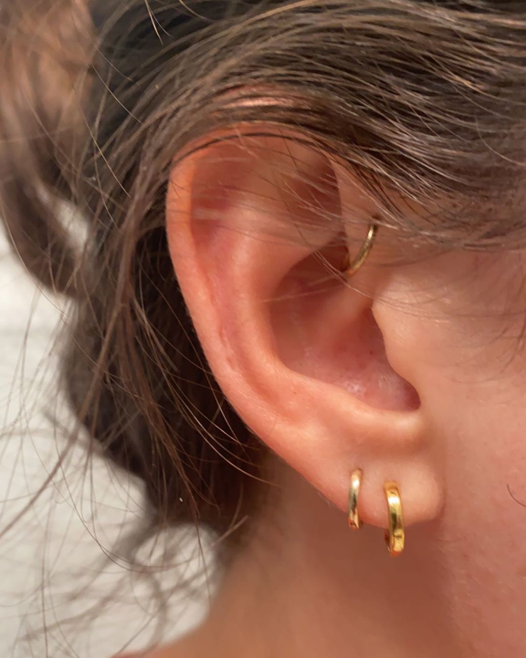 Close-up of an ear wearing two small gold huggie hoops in the lobe and one in the helix
