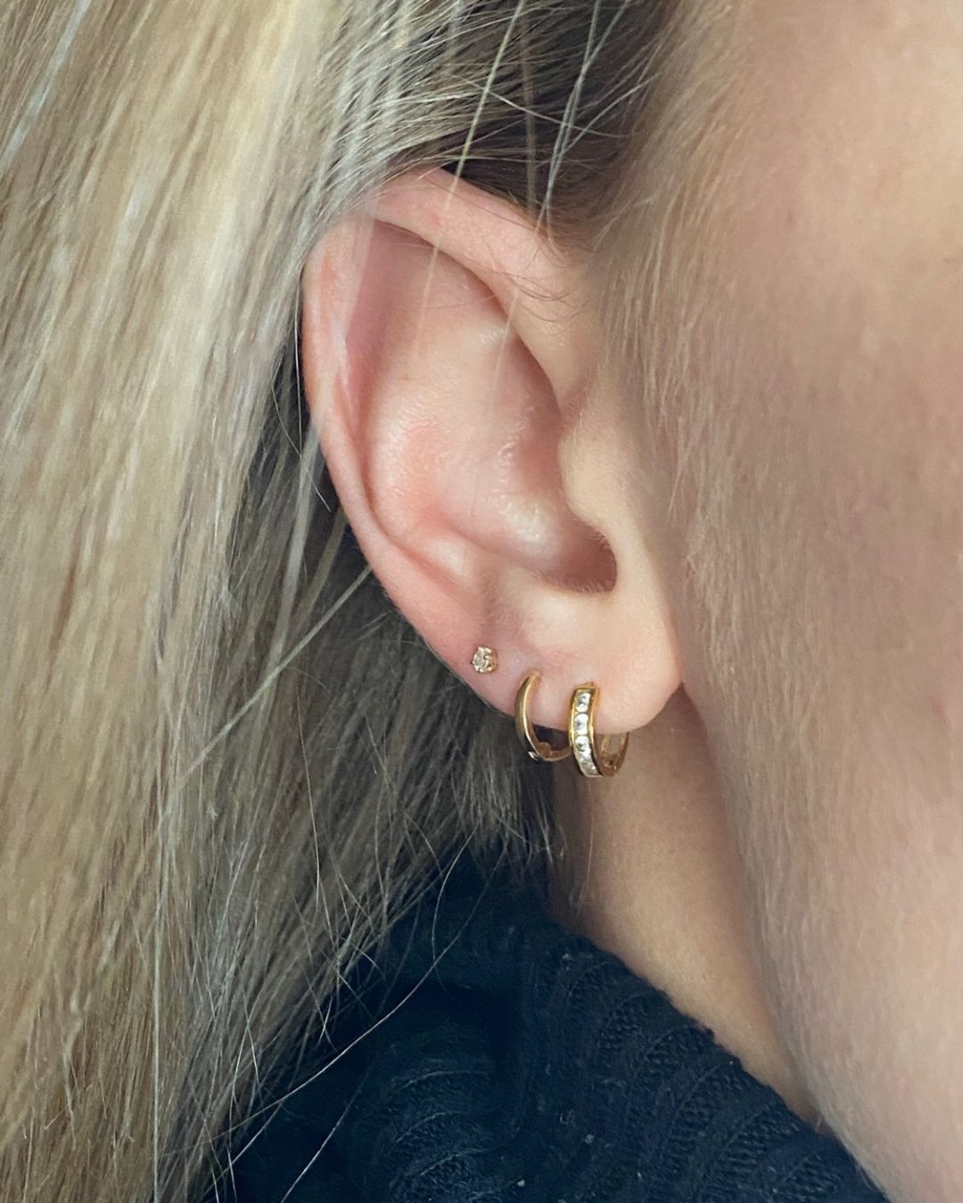 Close-up of an ear wearing a plain gold huggie hoop, a crystal-set hoop and a small stone stud