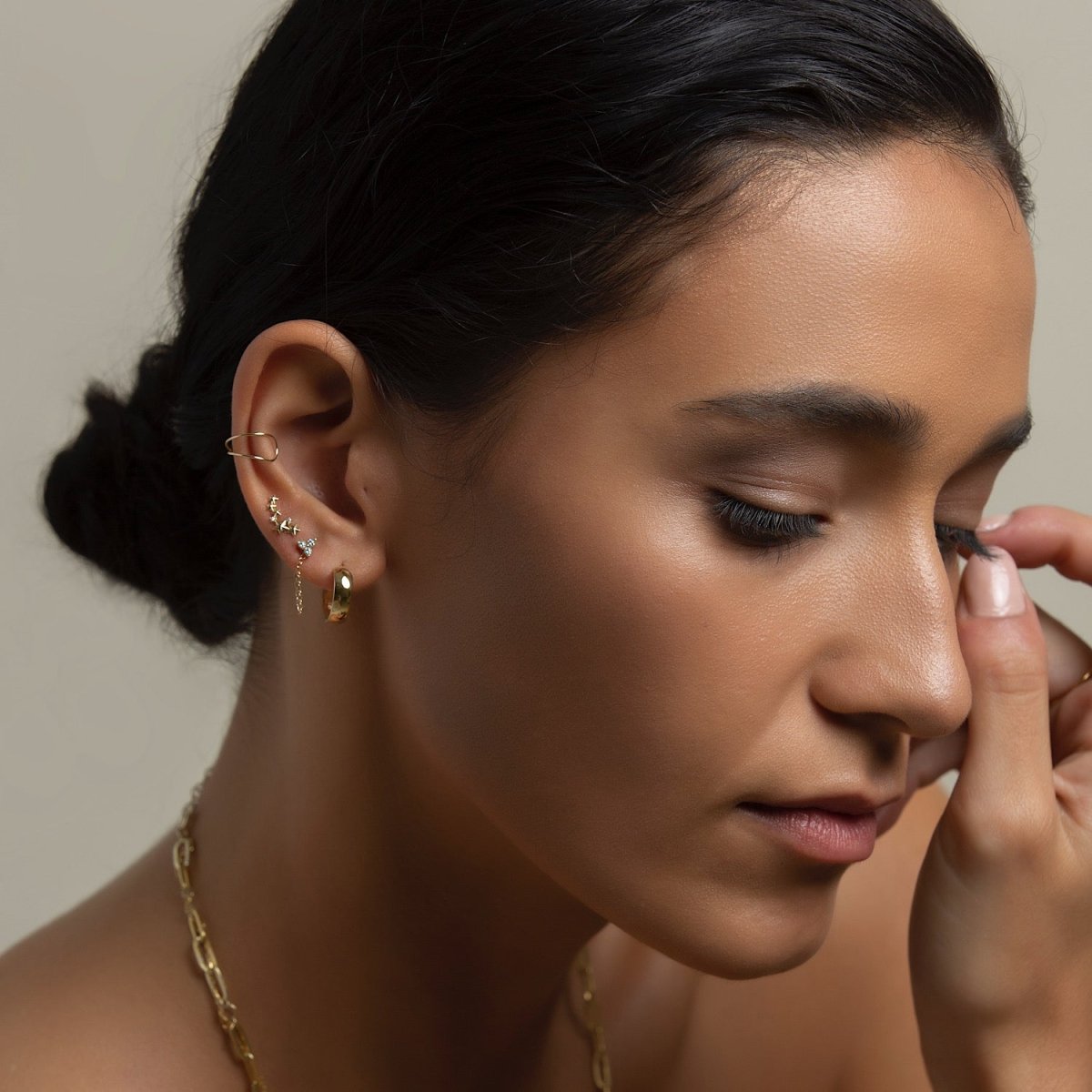 Close up of woman's ear featuring Gold Vermeil Tiny Clover Pave Studs, star stud, gold hoop earring, and ear cuff