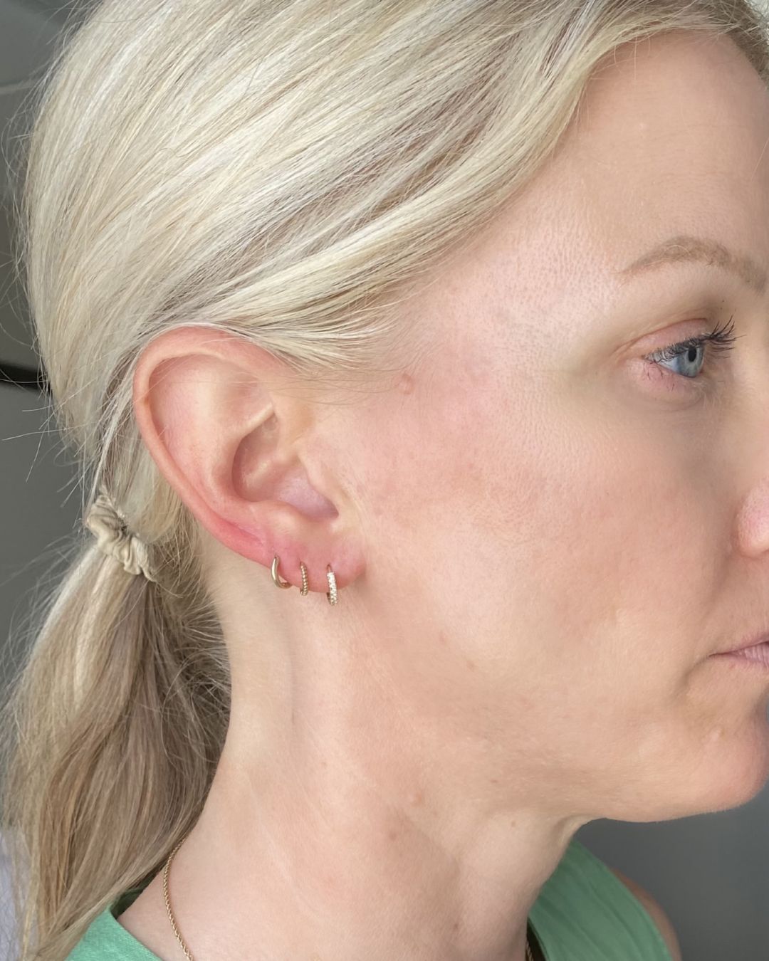 Side profile of a model's ear wearing three small gold huggie hoops in stacked lobe piercings