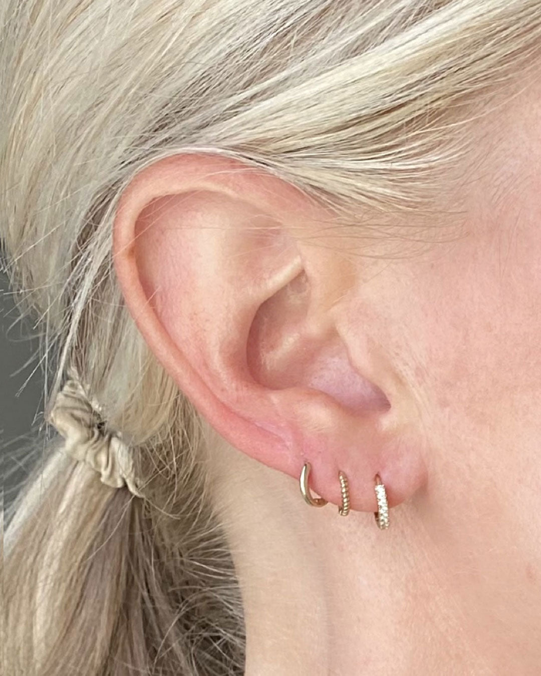 Close-up of an ear wearing three small gold huggie hoops in the lobe, one set with tiny crystals