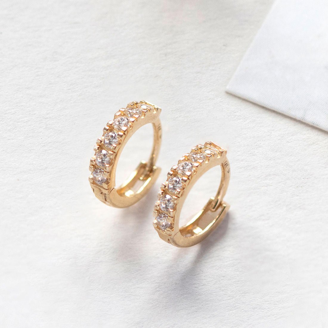 Close-up of 14K gold moissanite crysta pave huggie earrings.