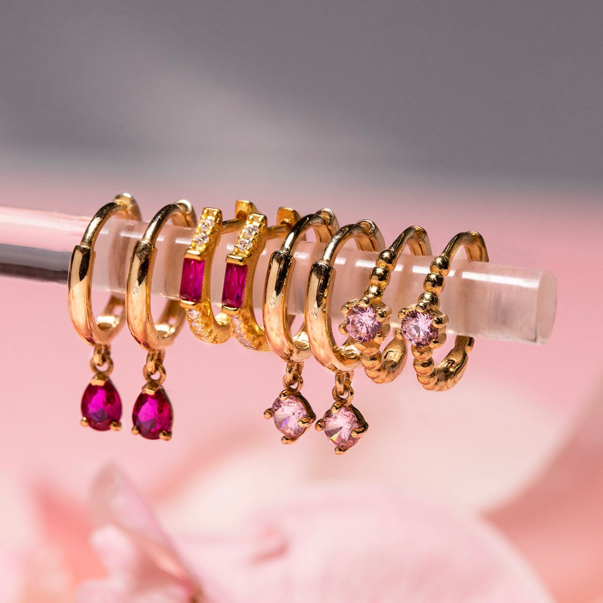 Close-up on earrings featuring 14K Gold Gemstone Dangle Huggies Pink + Ruby CZ Crystal