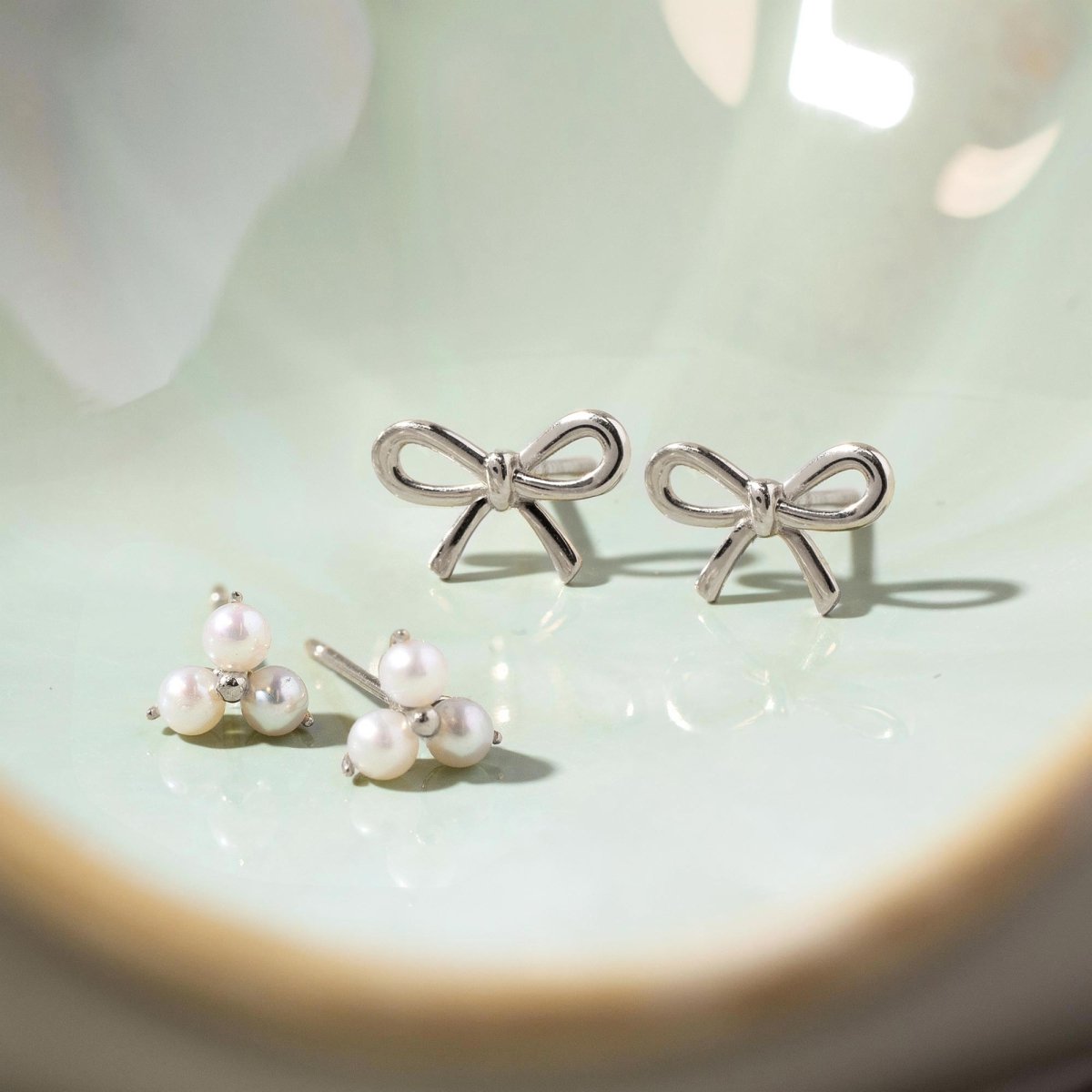 Close up of earrings featuring 14K White Gold Bow Studs and pearl clover studs
