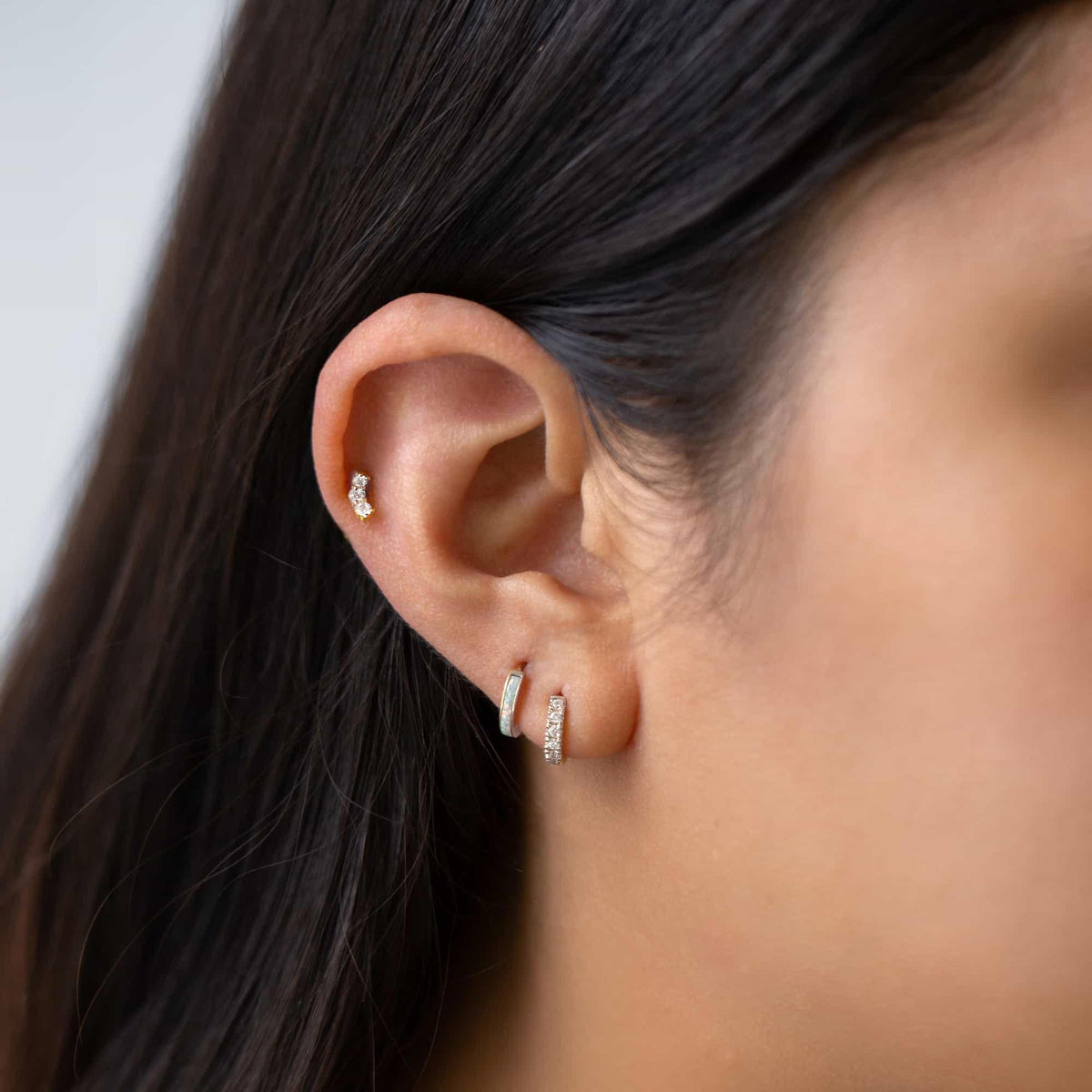Close-up on woman featuring sterling silver moissanite crystal huggie and opal huggie earrings.