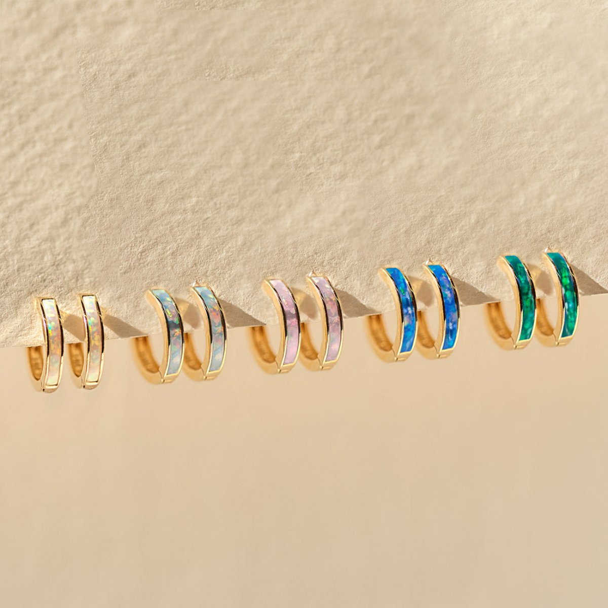 Set of gold hoop earrings with colorful stones on a beige background