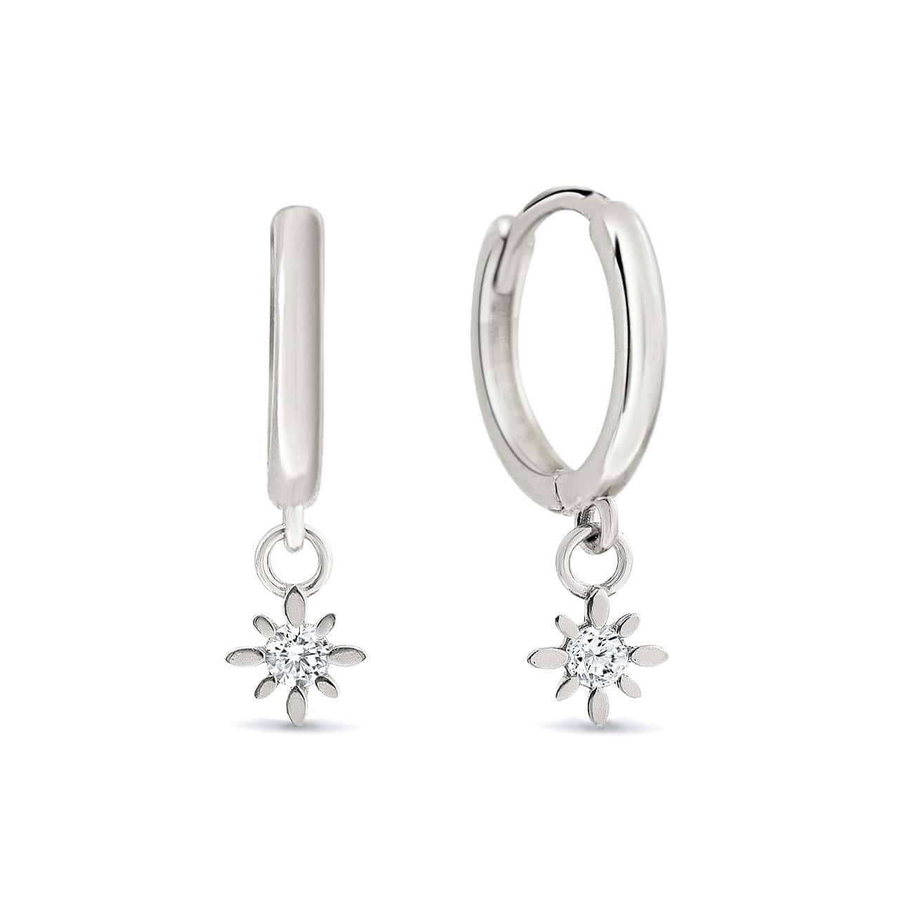 Pair of 14K white gold huggie hoops with dangling starburst charms set with clear zirconia, on a white background