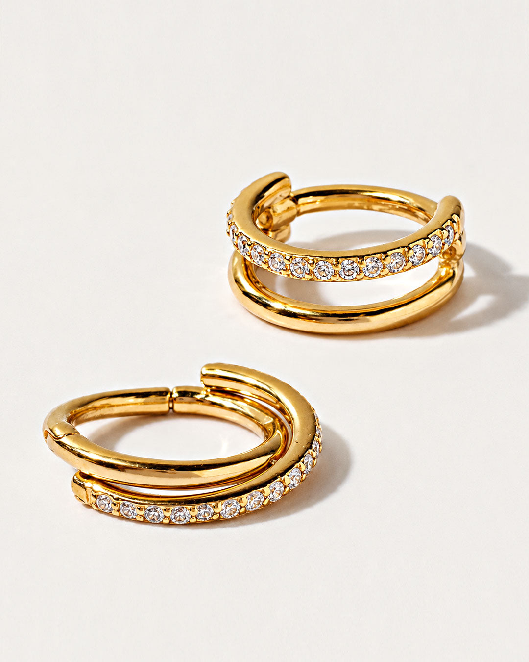 Discover AMYO cartilage earrings with sleek layered gold hoops and shimmering crystal accents.
