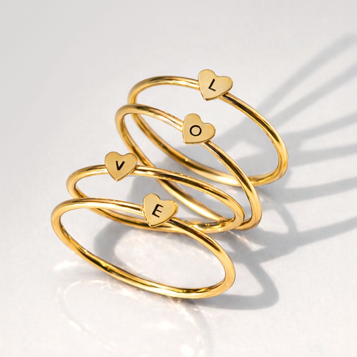 Set of gold heart-shaped rings from AMYO spelling 'LOVE' on a light background