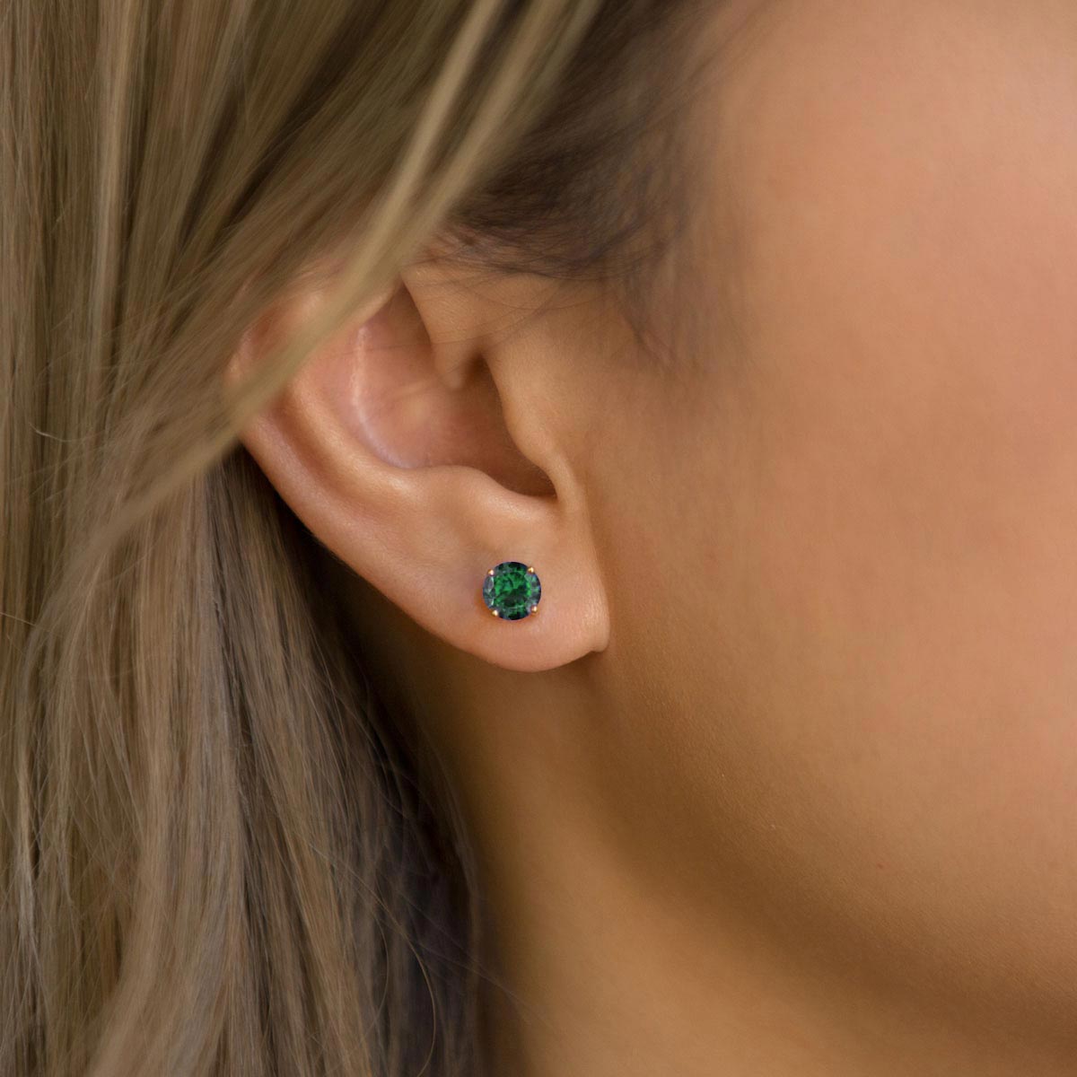 Sterling Silver emerald stud with a round green stone shown on a model's earlobe