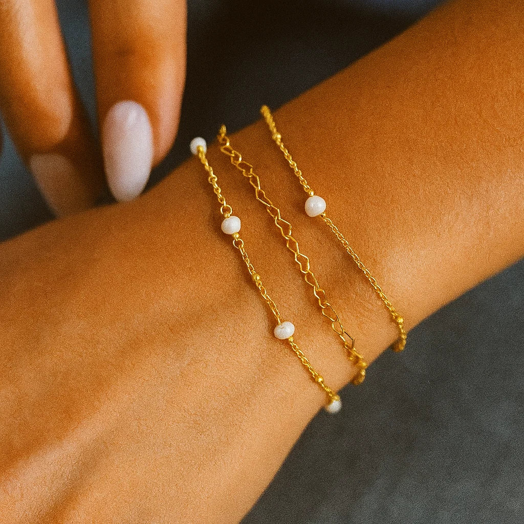 AMYO Gold chain bracelet with pearl beads on a wrist against a dark background