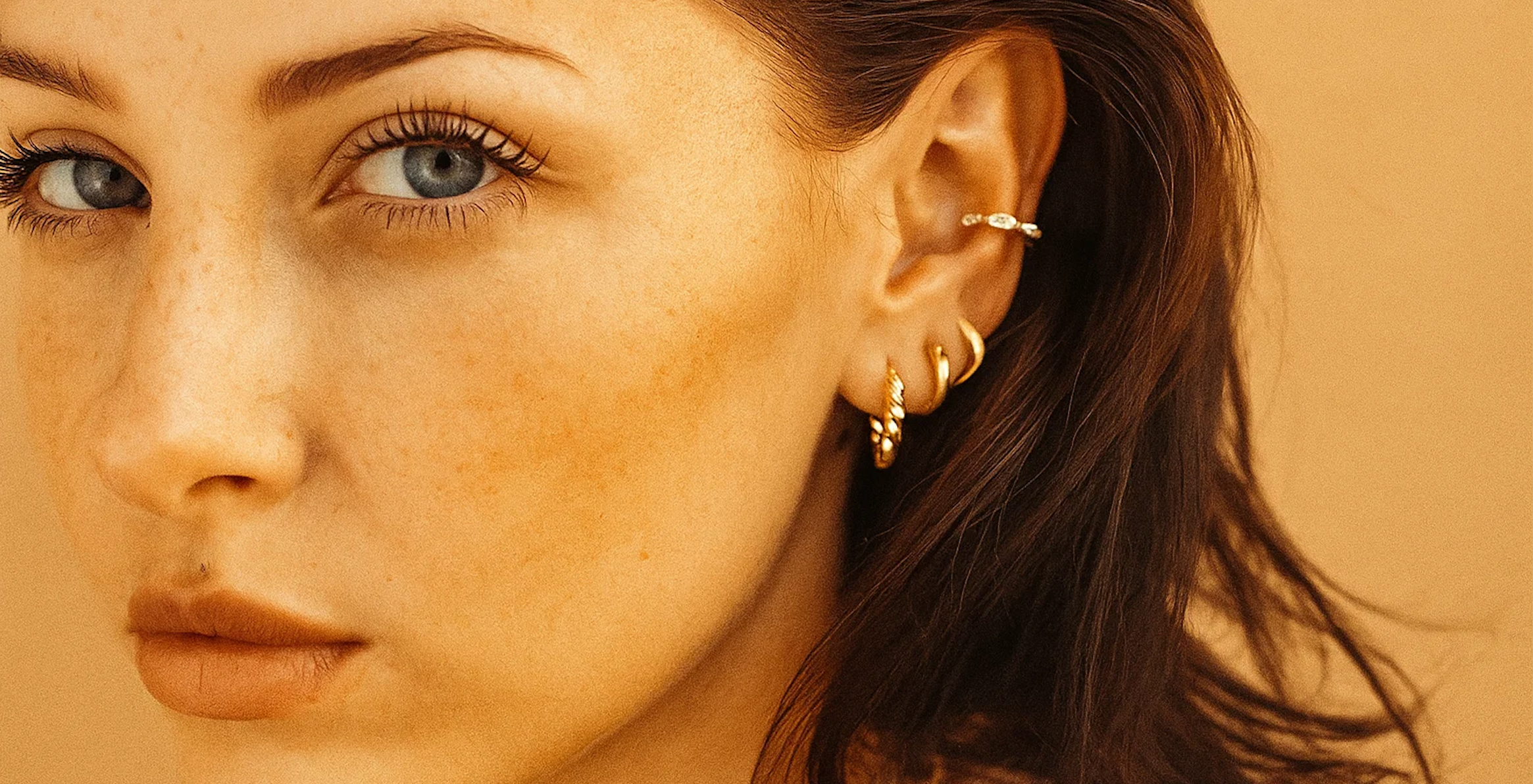 Close-up of a woman's face wearing AMYO gold earrings against a beige background