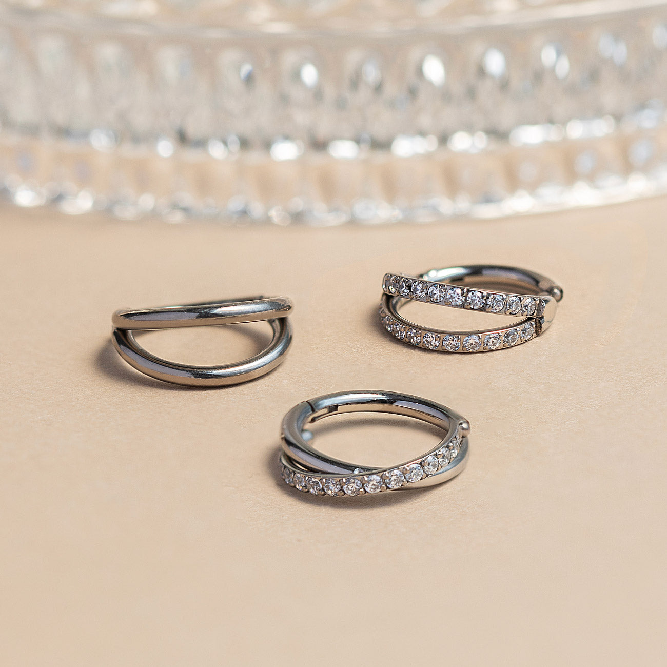 Three AMYO silver hoop earrings with embedded stones on a beige surface.