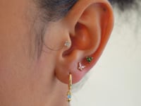 Close up of woman's ear featuring gold huggies and gemstone stud earrings.