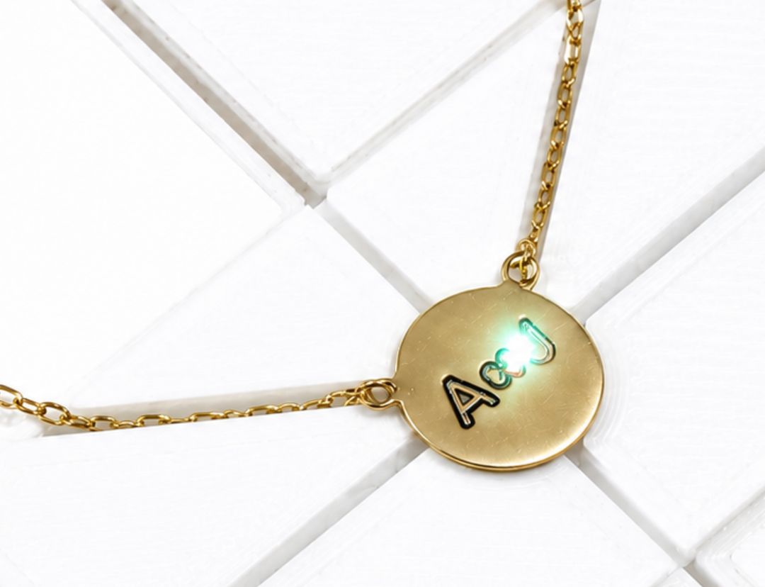 Gold round disc pendant engraved with initials, on a fine chain resting on white tile