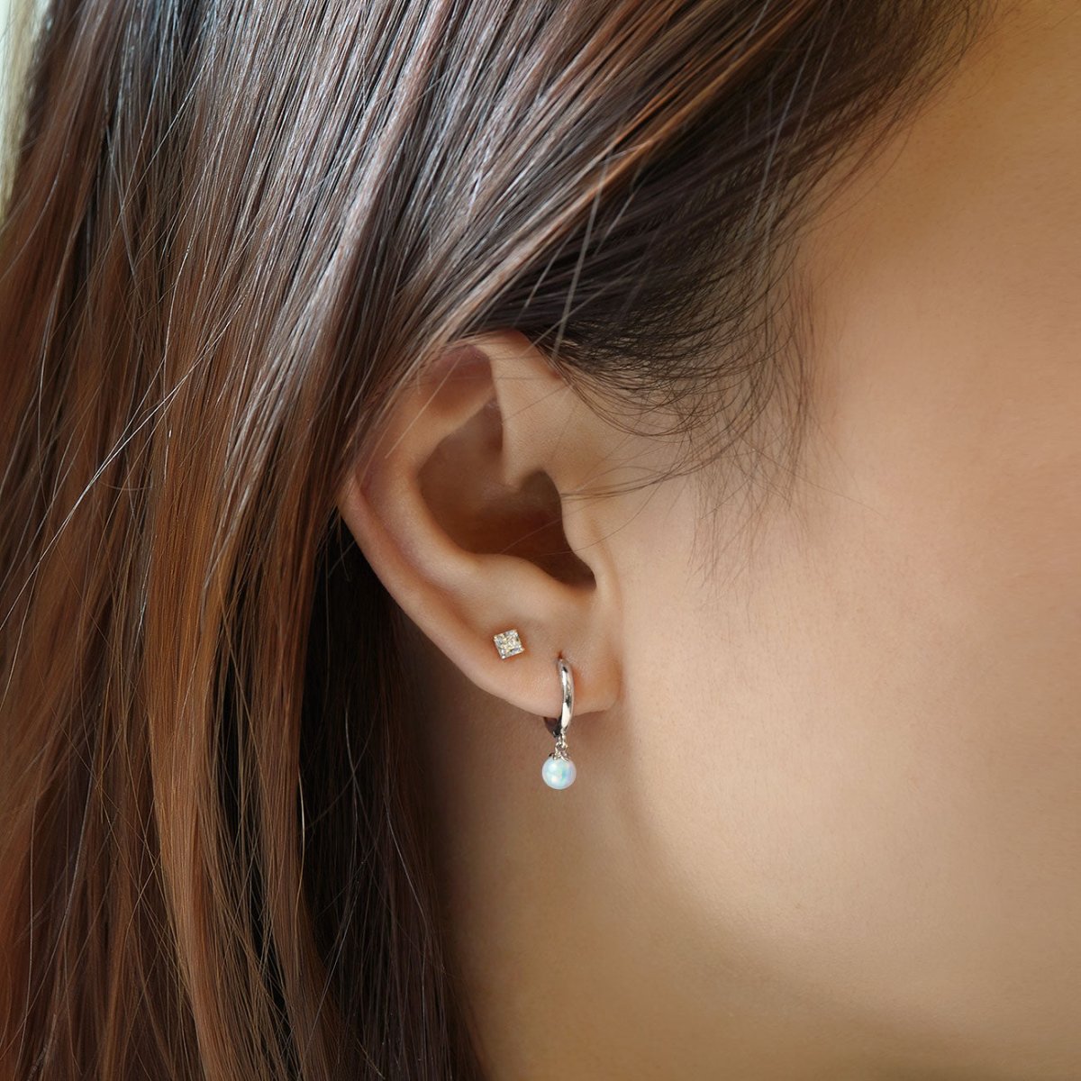 Close-up of woman's ear featuring 14K White Gold Tiny Opal Huggies paired with stud earrings