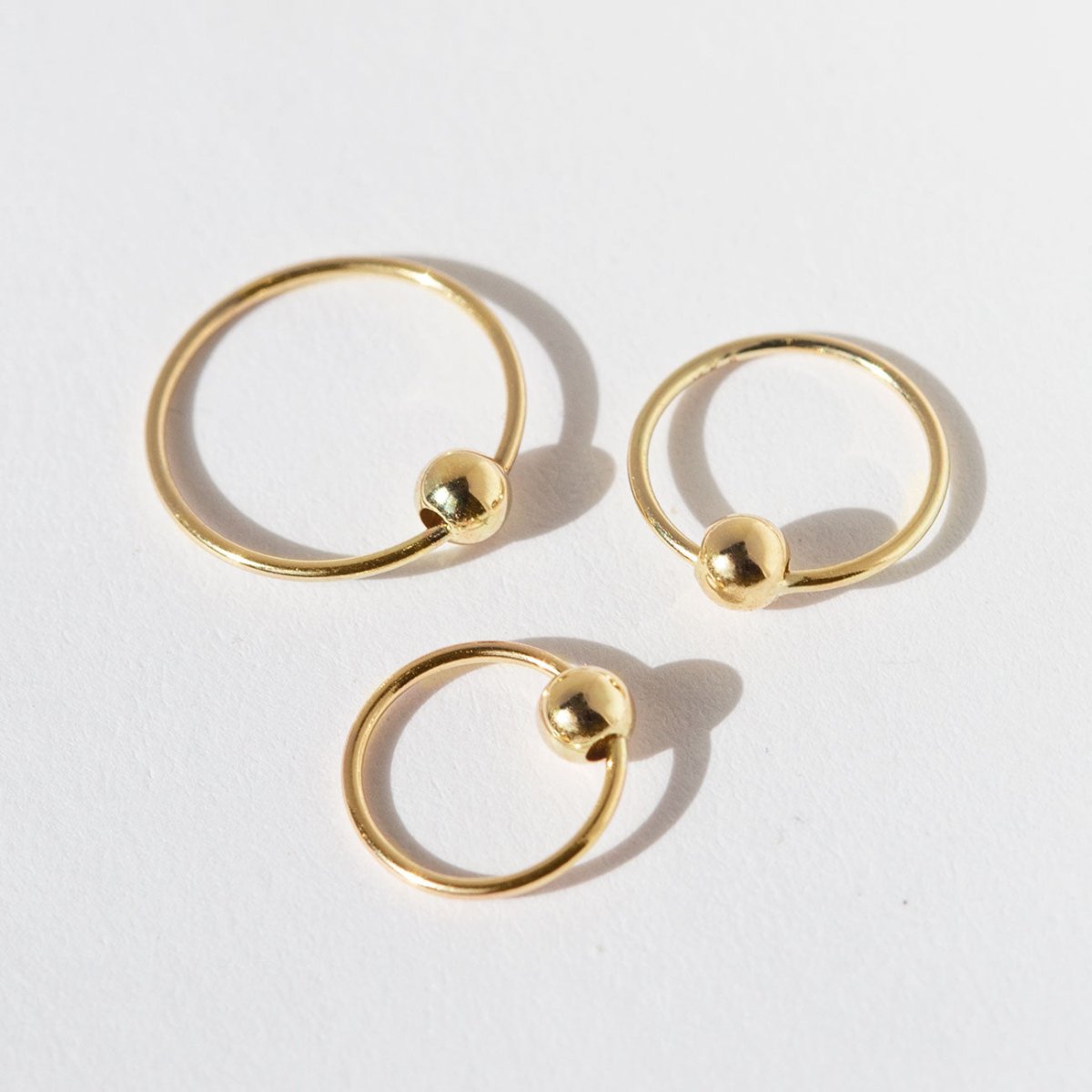 Three 14K gold captive bead rings in graduated sizes, shown together on a cream background