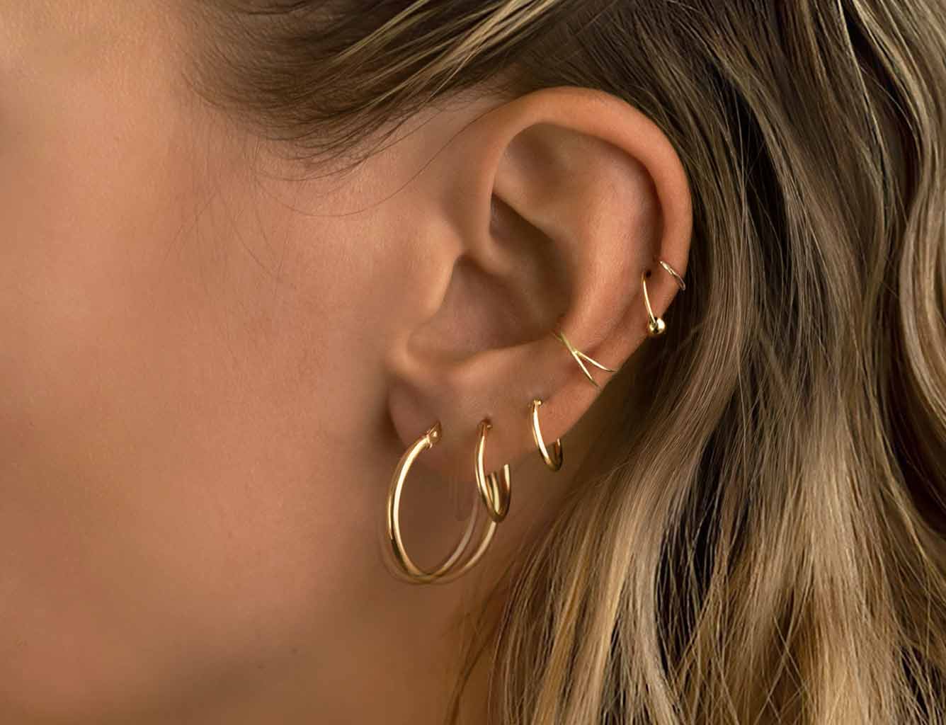 Close-up of multiple 14K gold cartilage hoops and helix earrings styled together by AMYO Jewelry