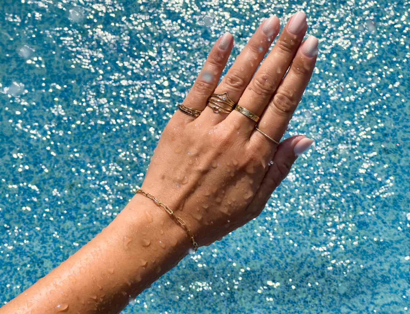 Woman’s hand wearing waterproof 14K gold rings and bracelet in water, showcasing AMYO Jewelry’s tarnish-resistant pieces.