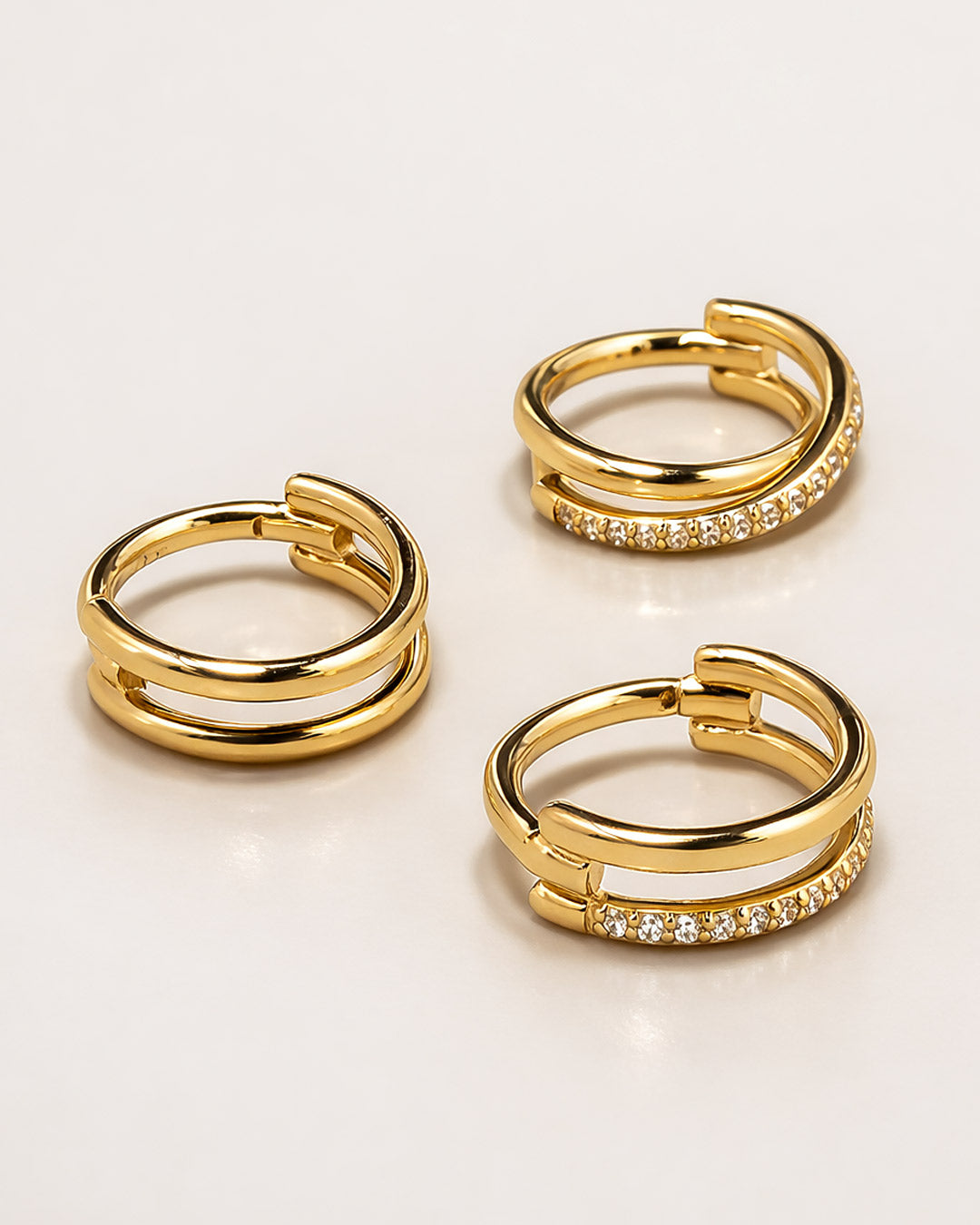 Three gold cartilage hoop earrings with embedded stones on a light beige background from AMYO.