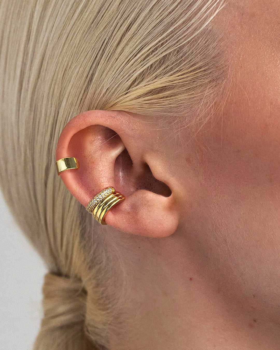 Ear styled with gold vermeil ear cuffs including stacked gold and pavé ear cuffs, worn along the cartilage and conch for a modern layered look. Links to AMYO Ear Cuff Collection.