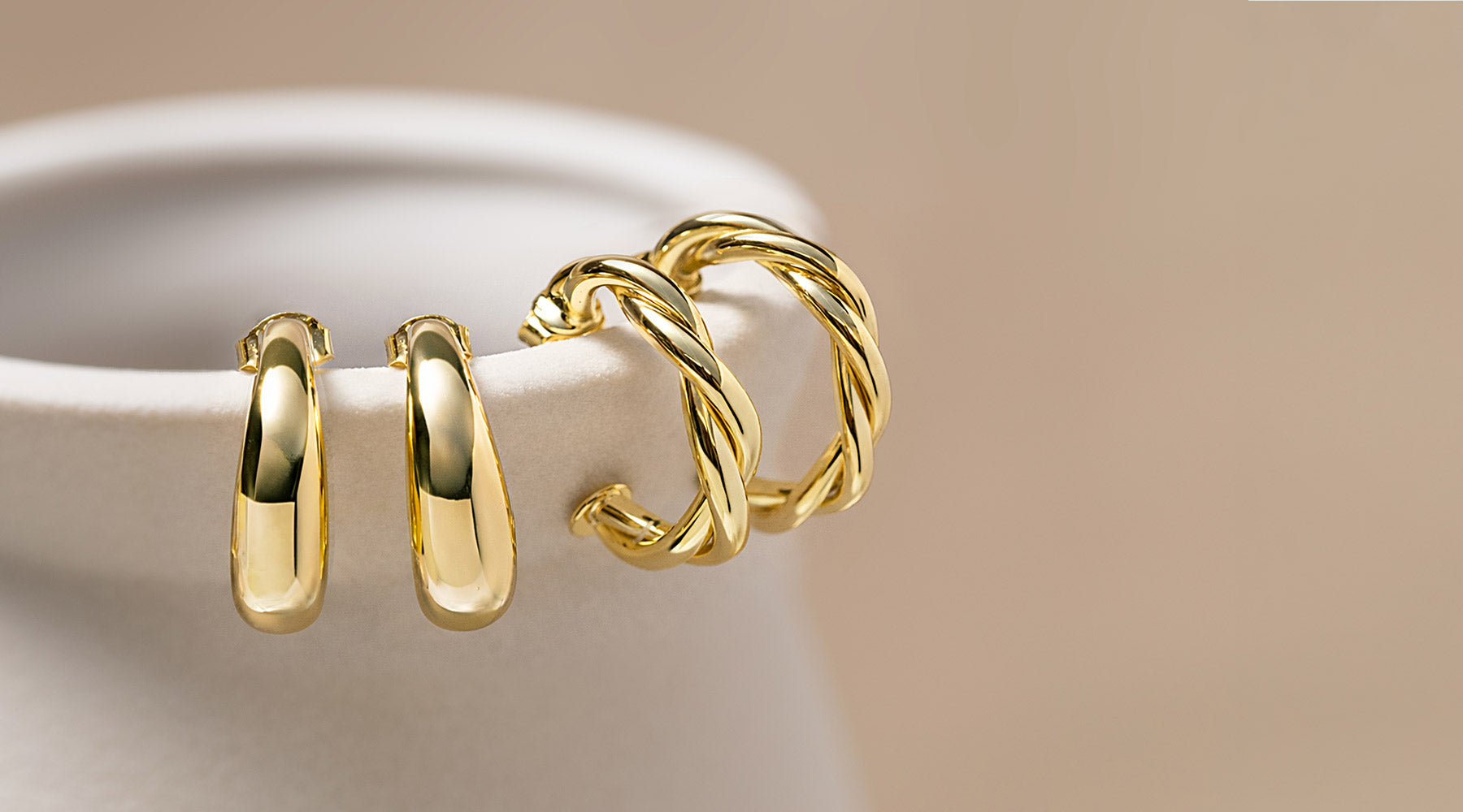 Polished and twisted gold vermeil hoop earrings styled on a vase, showcasing timeless hoop styles from the AMYO earrings collection.