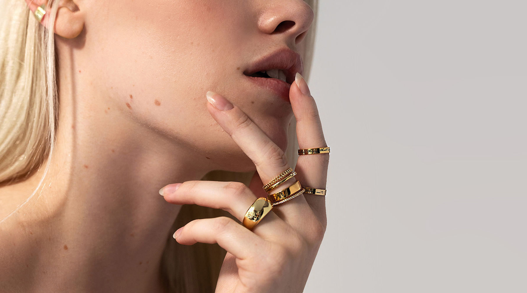 Hand wearing layered gold rings including engraved and thin and chunky stacking styles, linking to the AMYO rings collection.