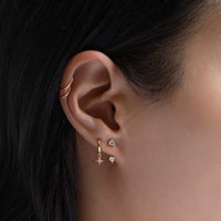 Close-up of woman wearing gold tiny solitaire earring jacket, gold star flare huggie earrings, and gold thin huggie hoops