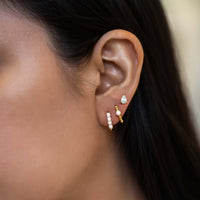 Close-up on woman's ear featuring Gold Vermeil Gemstone Bead Huggies Opal and studs. 