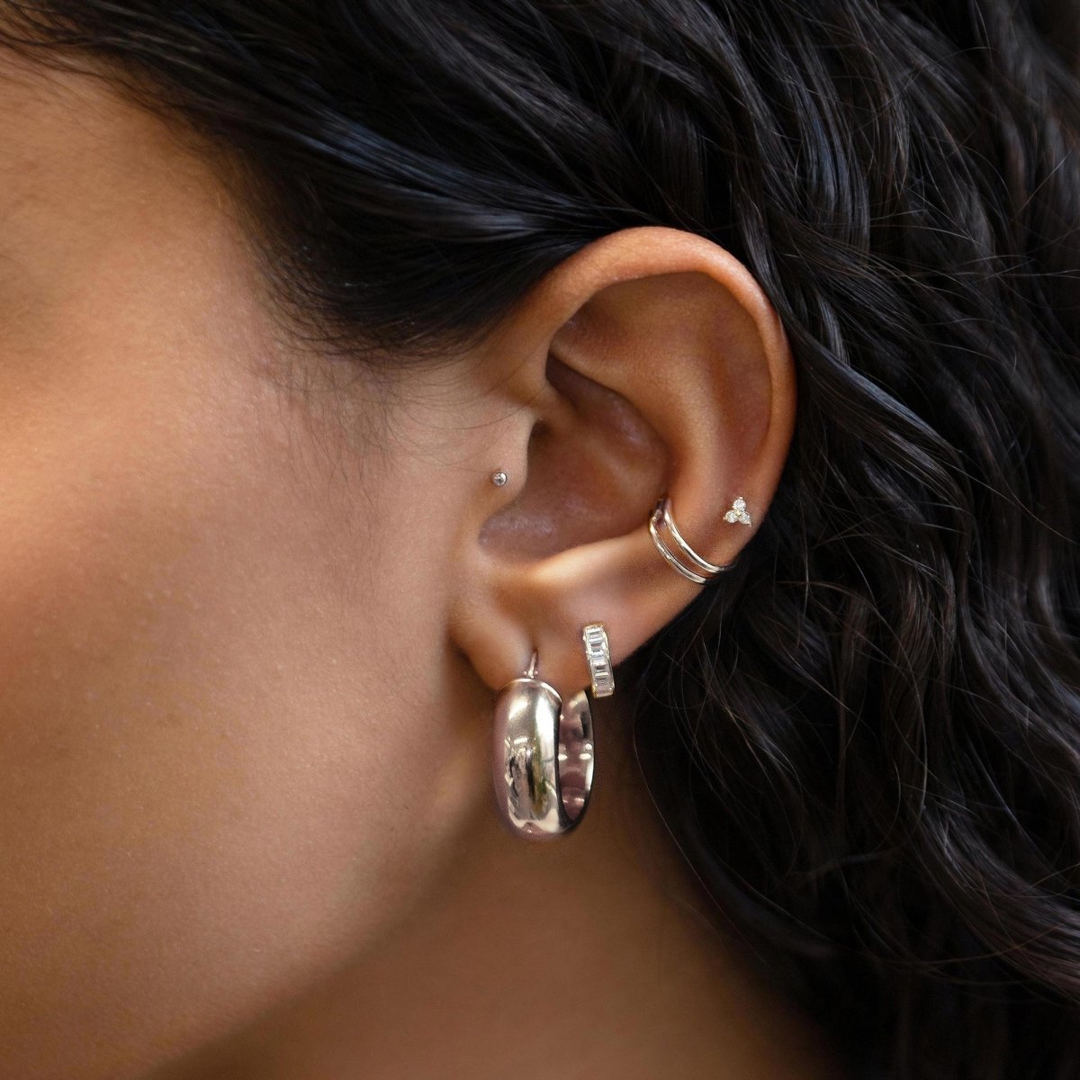 Close up of woman's ear featuring Pave Clover 14k white gold stud earrings and chunky silver hoop earring 