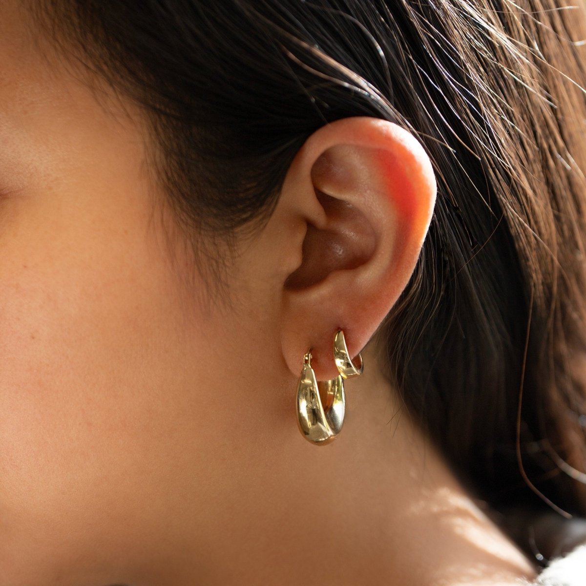 14K gold sculptural U-shaped bubble hoop earrings shown close-up on a model's lobe