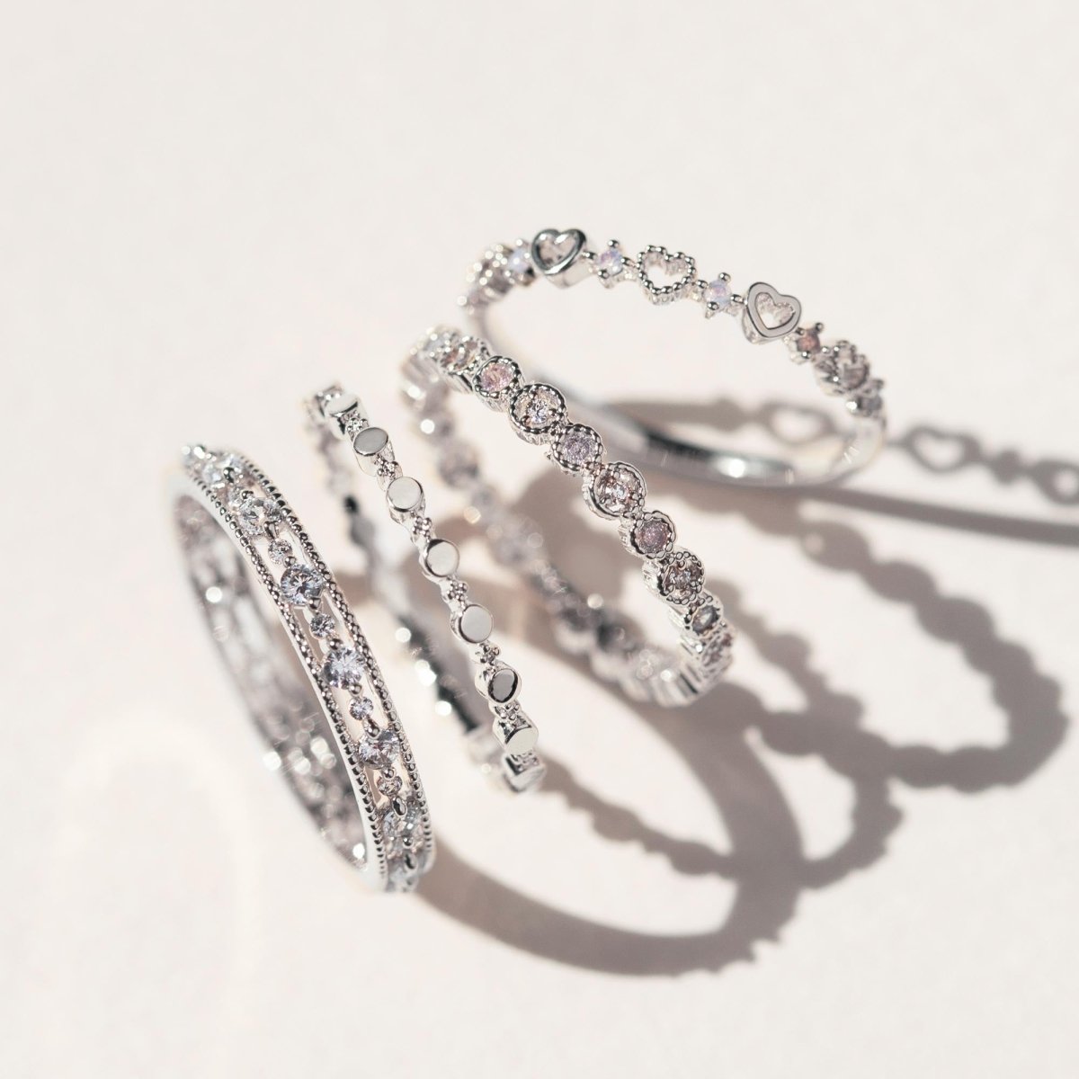 Four sterling silver stacking rings including a beaded white zirconia eternity band, on a cream background