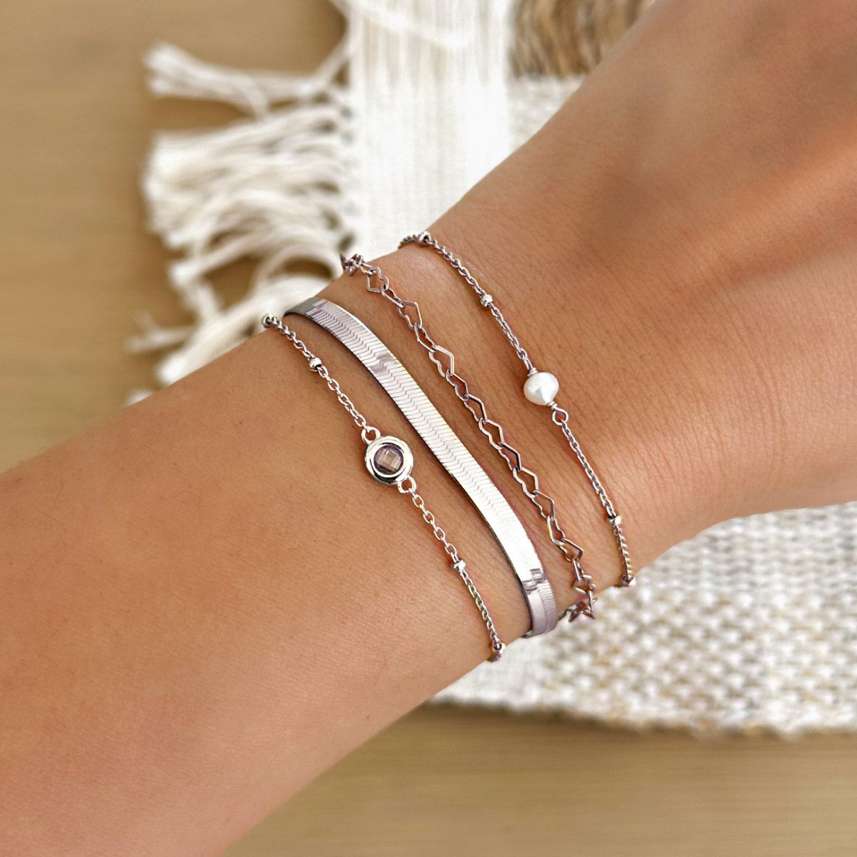 Close-up of a wrist wearing multiple sterling silver stacking bracelets featuring pearls, crystals, hearts from AMYO