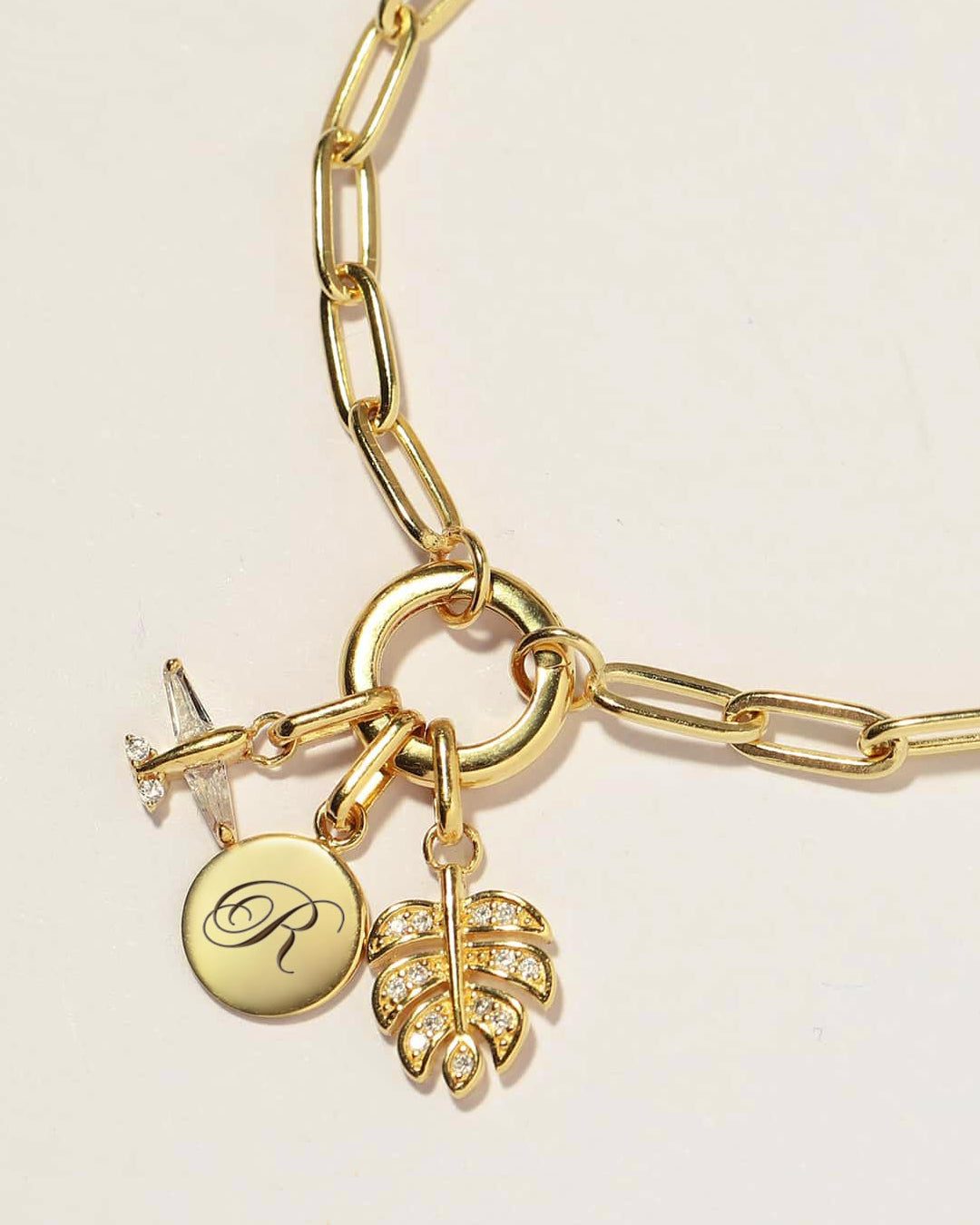Gold bracelet with engraved initial charm, pavé leaf, and airplane charm – shop customizable charms for gifting and layering.