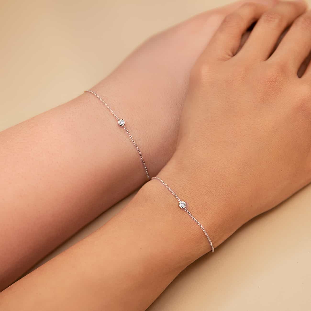 14K white gold bezel diamond chain bracelets shown on two model wrists on a cream background