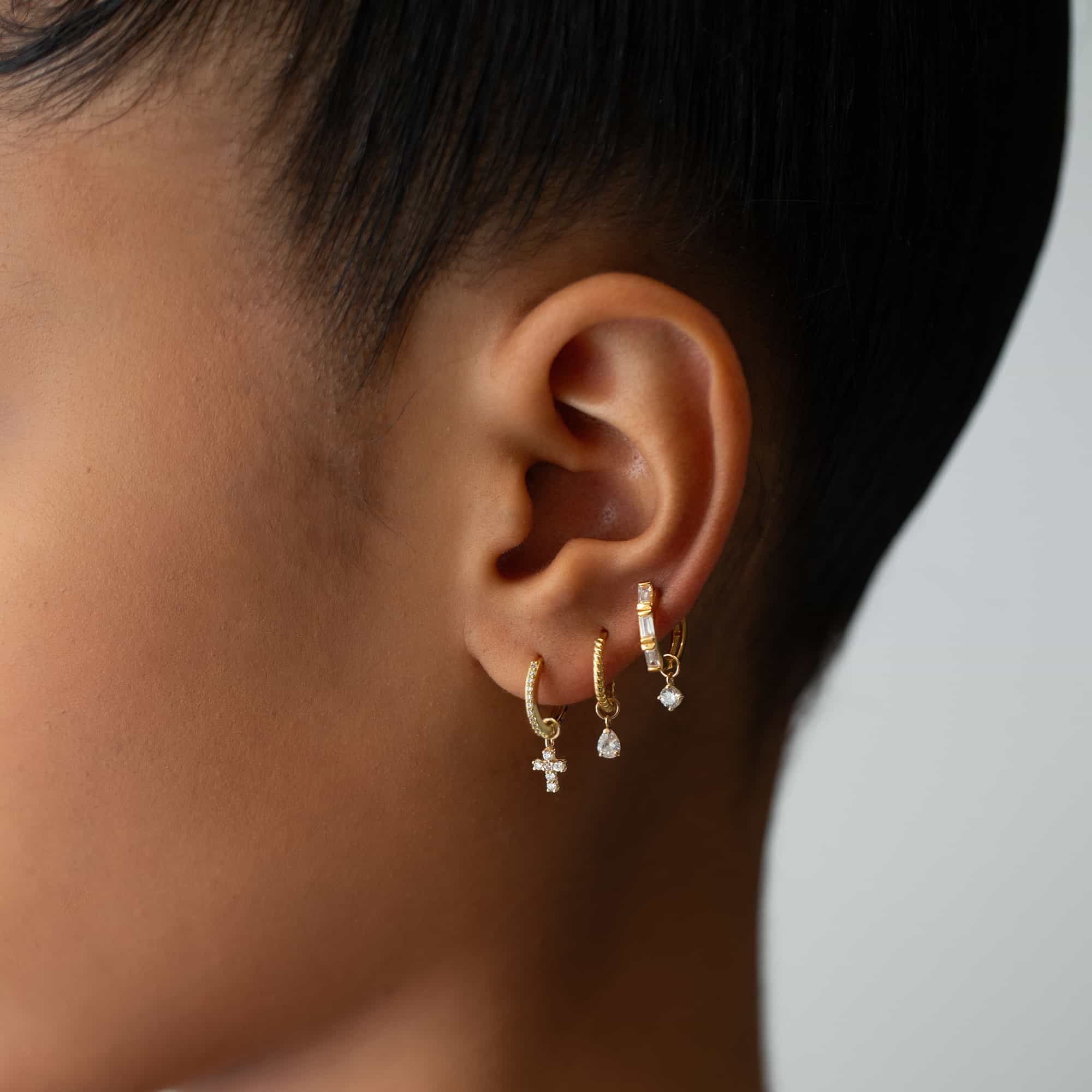 Close-up of woman's ear featuring 14K Solid Gold Tri Baguette Huggie Hoops Moissanite Crystals snd other huggie charm earrings