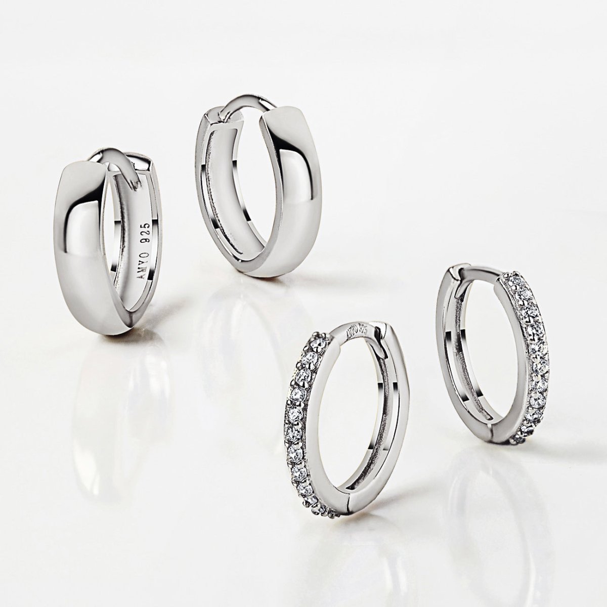 Two pairs of silver huggie hoops on a white surface, two plain and two lined with small crystals