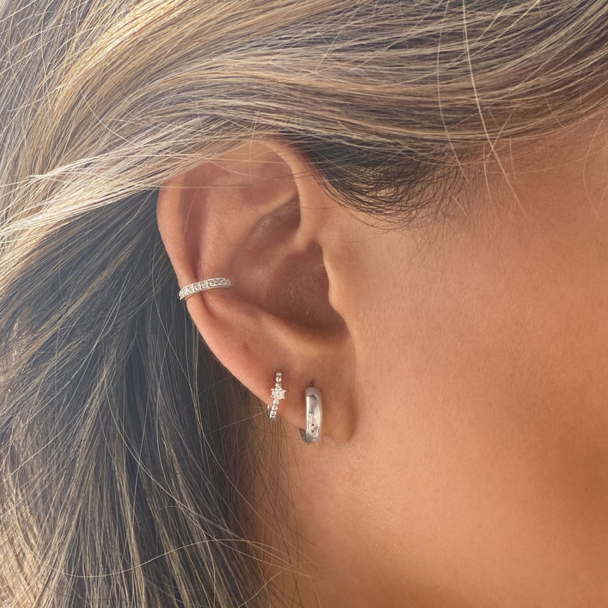 Close-up of woman's ear featuring  Sterling Silver Pave Bead Huggie Earrings CZ Crystals, Gold Chunky Hoop, & Cuff. 