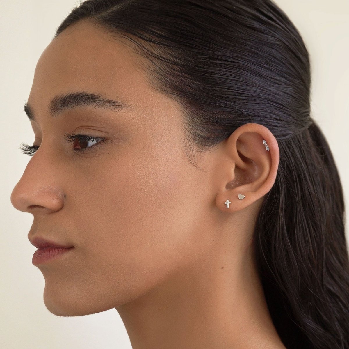 14K white gold pavé zirconia cross stud shown on a model's lobe, side profile