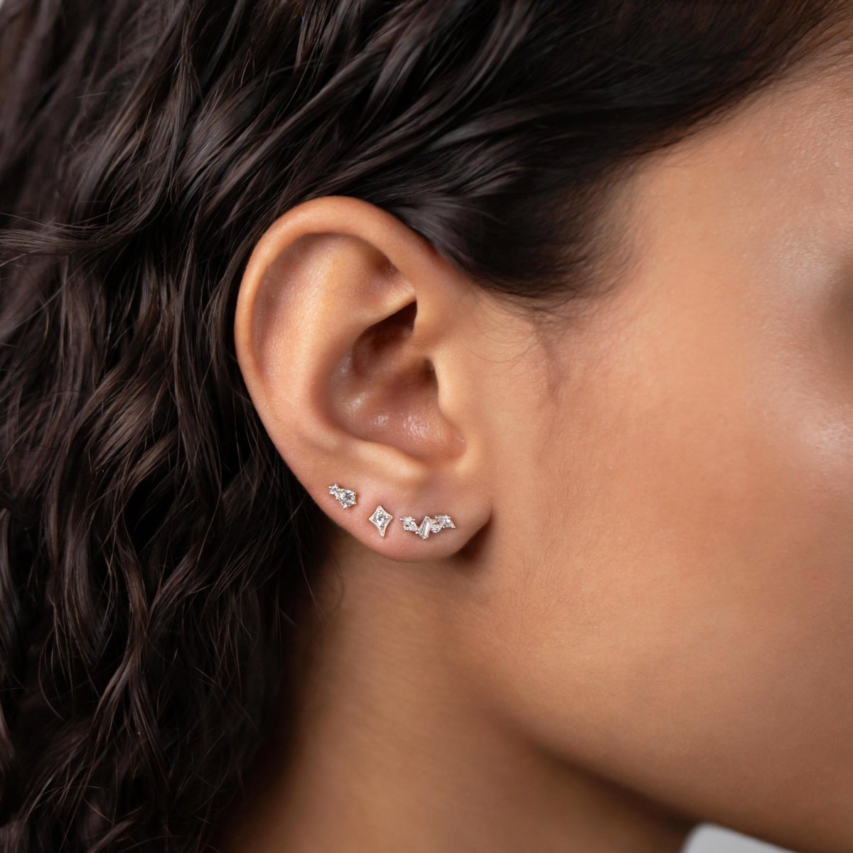 Sterling silver cluster studs with white zirconia stones in a row along a model's lobe